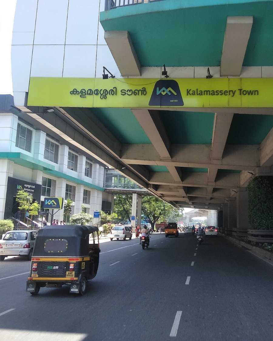 The road under the elevated Kalamassery Town metro station, with an auto-rickshaw passing.